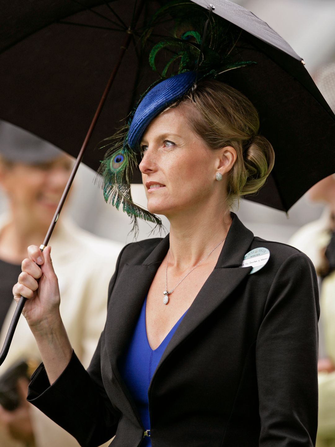 woman wearing peacock hat and holding umbrella 