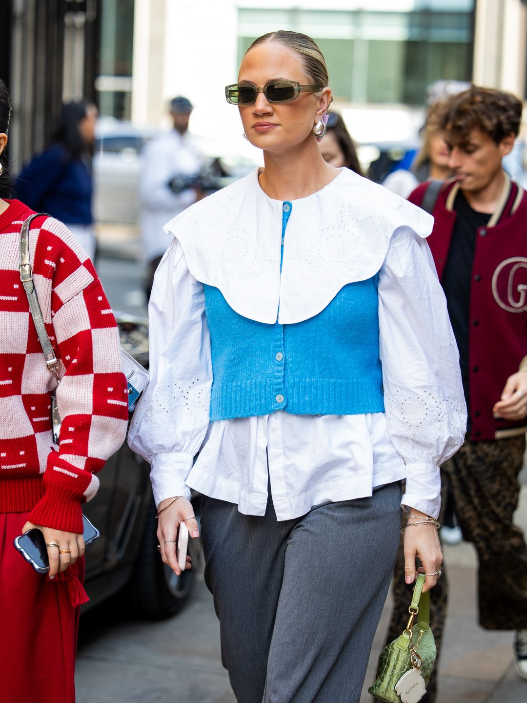 A guest wears white blouse, blue cardigan, grey pants, green bag outside JW Anderson during London Fashion Week September 2024 on September 15, 2024 in London