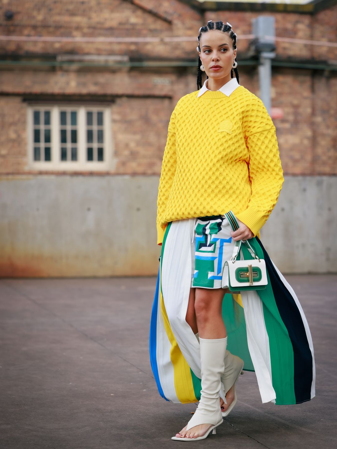 Fleur Egan wearing a yellow jumper, green and blue mixed colour maxi split skirt, white boots and green and white bag during Australian Fashion Week.