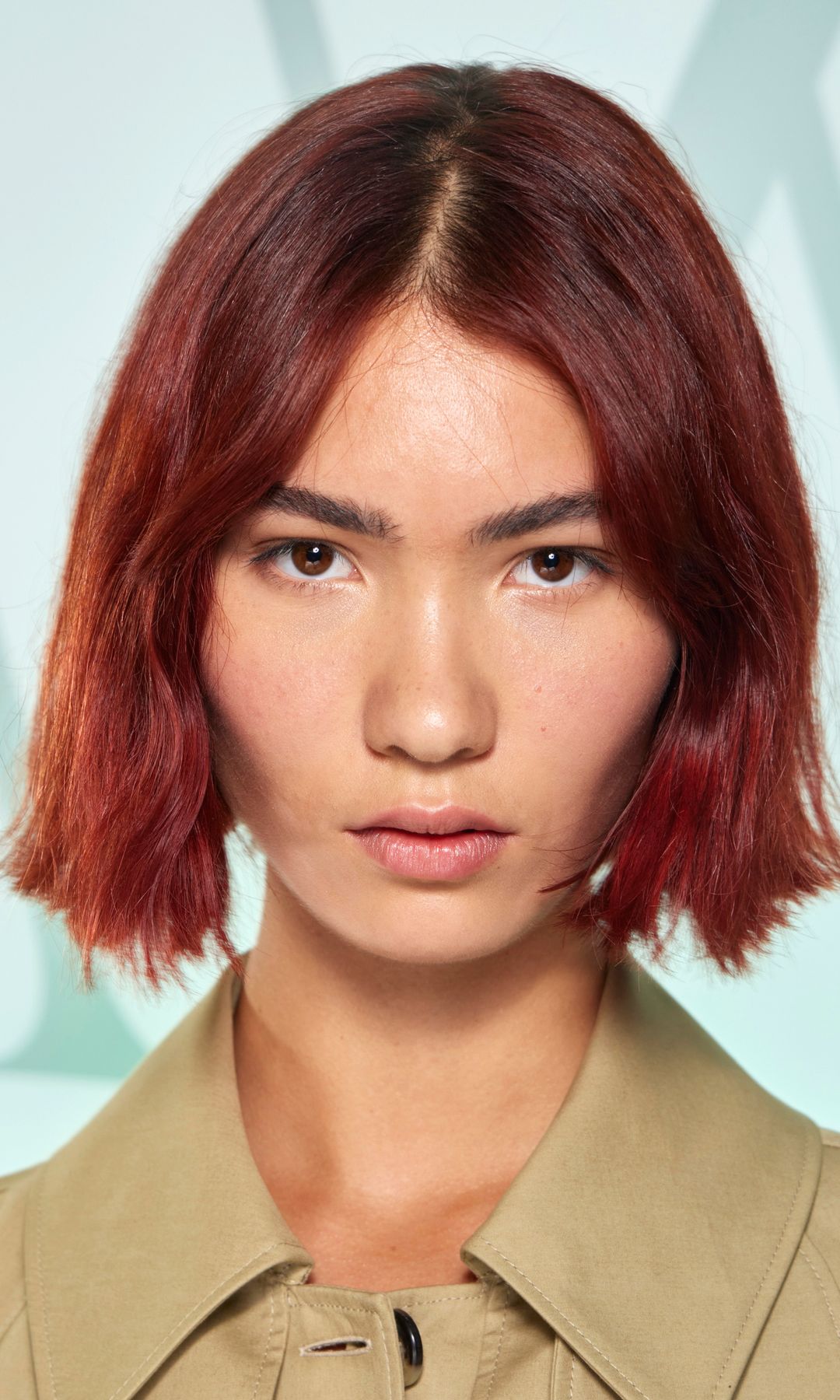 A model looks to the camera, she has a sharp blunt bob in a rich cherry-cola shade