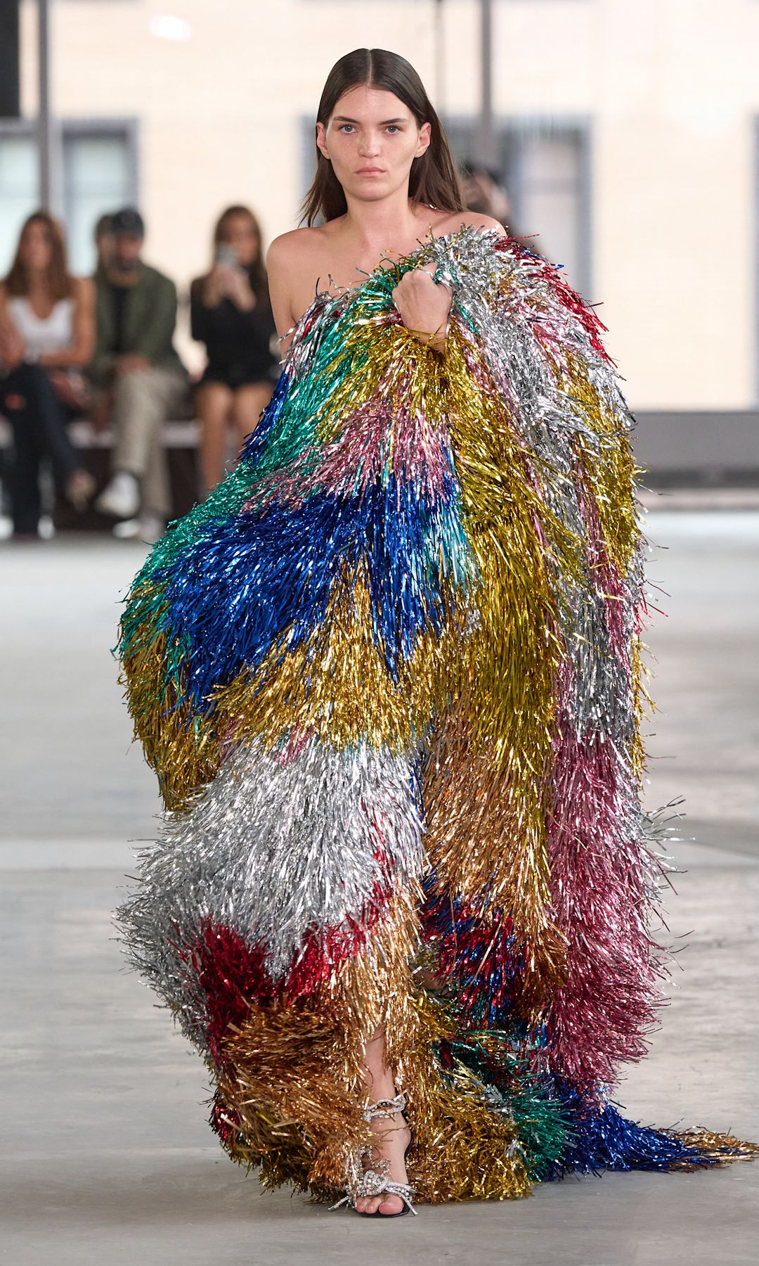 A model walks down the runway in a huge tinsel outfit in multi colours