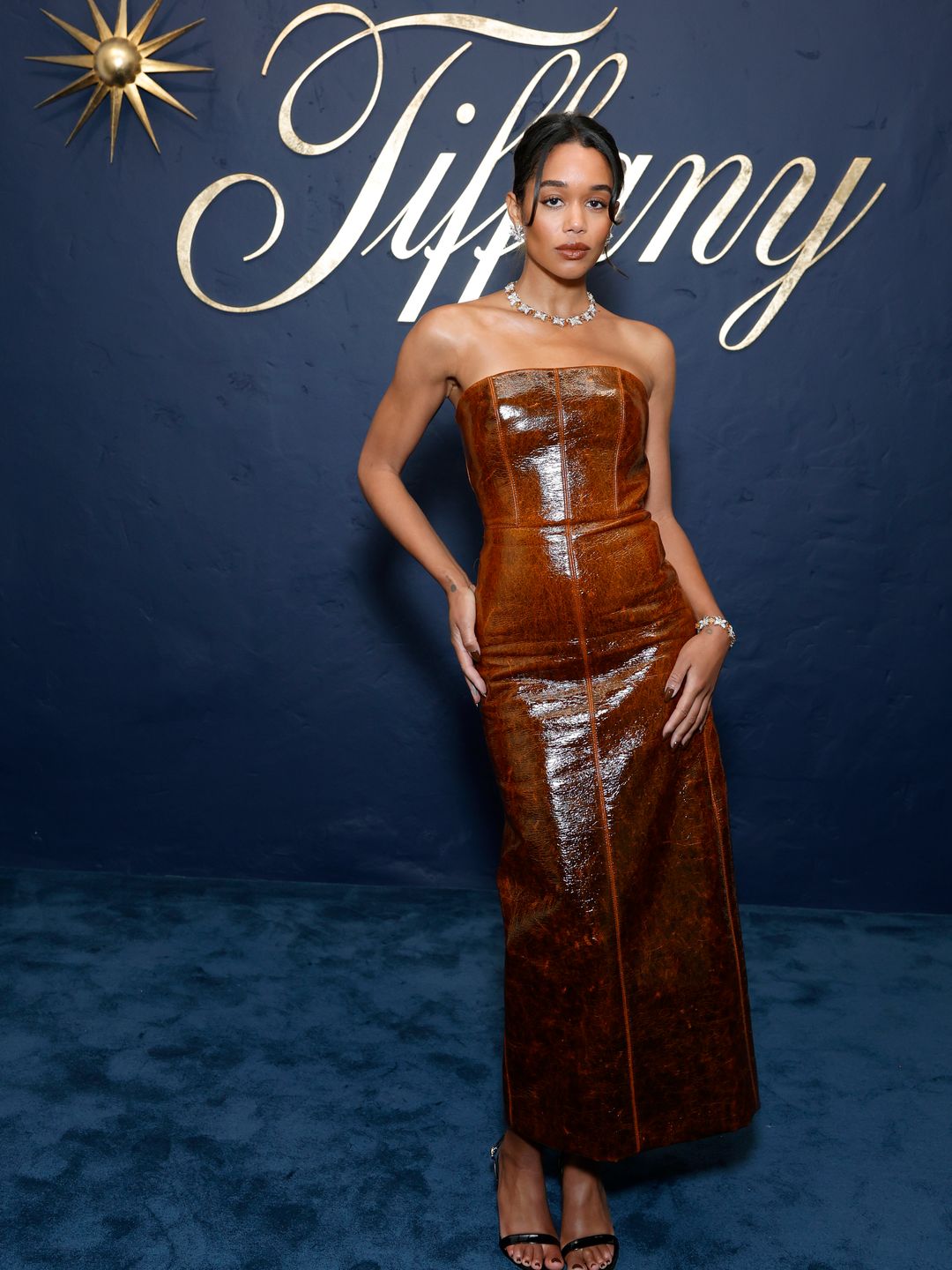 Laura Harrier attends the Tiffany & Co. Celebration of the launch of Blue Book 2024 in a strapless patent brown midi dress