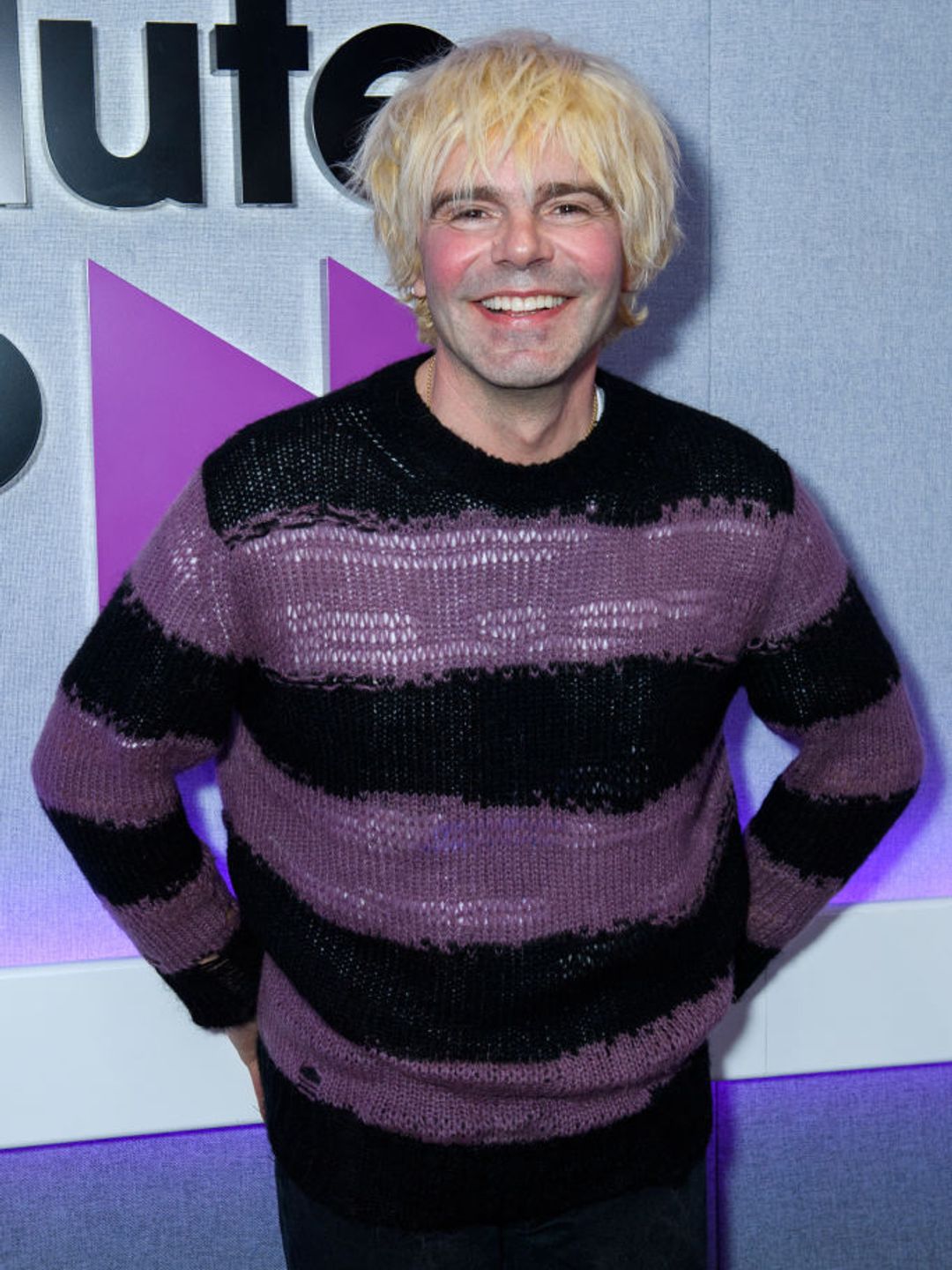 Tim Burgess smiling in a purple and black striped jumper.