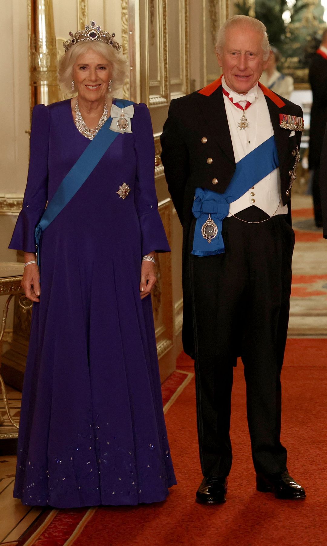 Queen Camilla in a purple gown and King charles in a black dinner suit