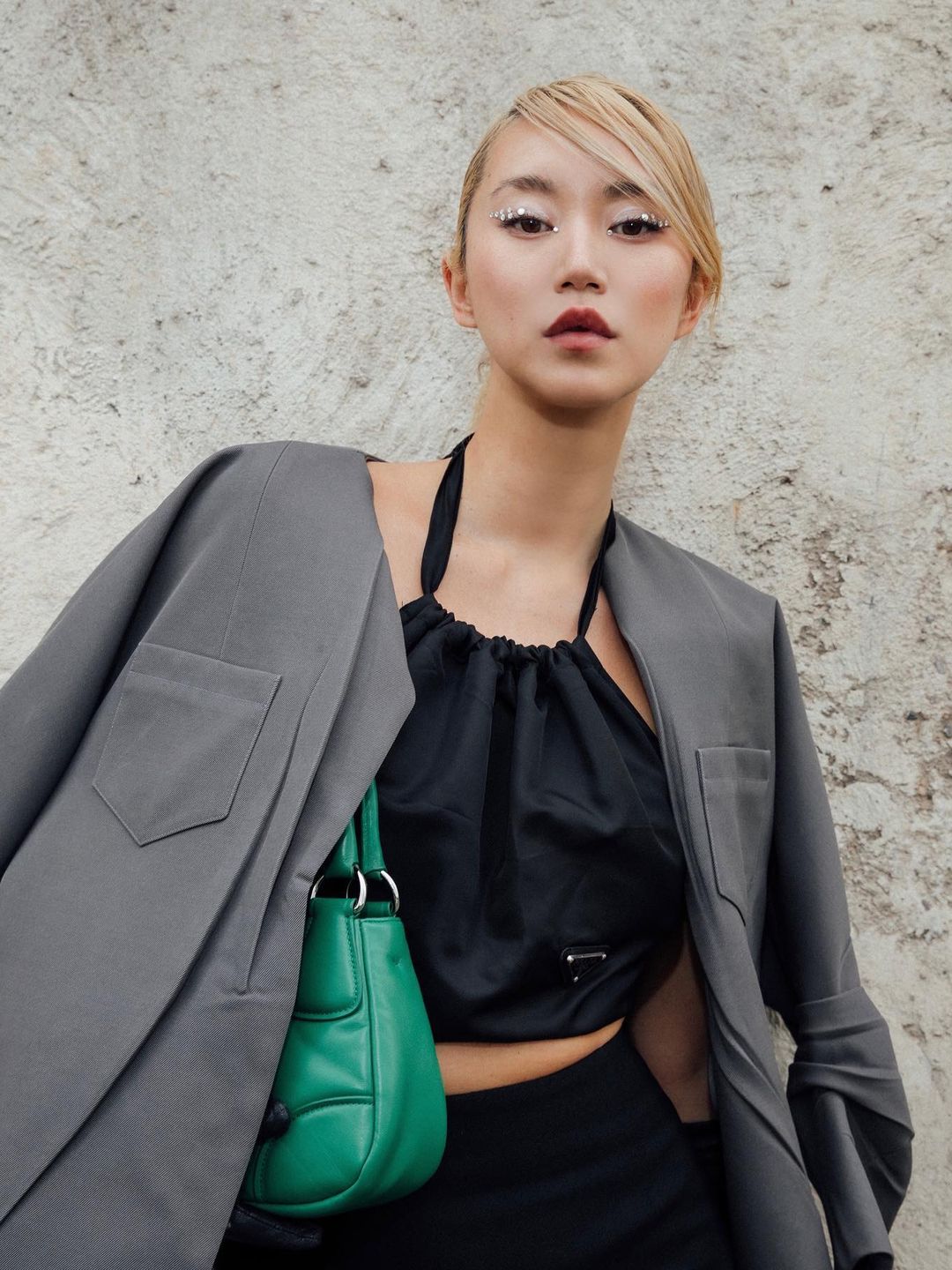 Influencer and style mogul Betty Bachz poses in a grey blazer with a green bag 