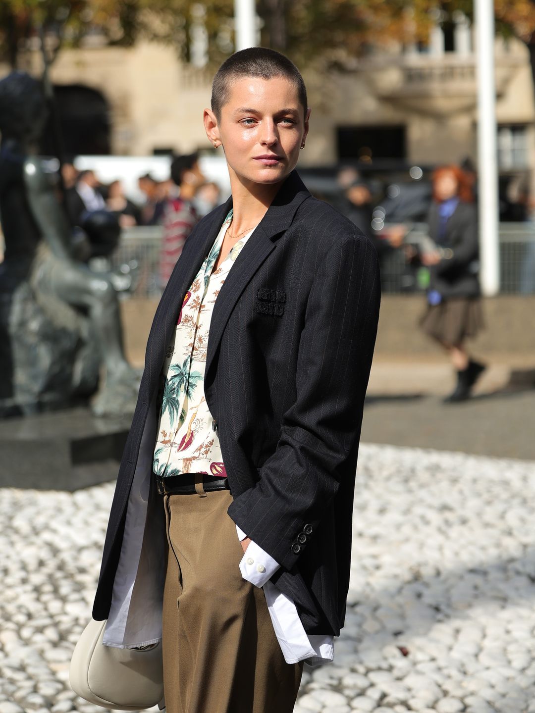 Emma Corrin at the Miu Miu runway show in Paris, wearing a black pinstripe blazer with tropical shirt and taupe trousers. 