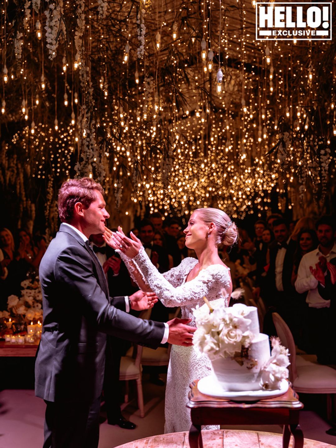 Amelia Spencer hugging Greg Mallett in front of their wedding cake