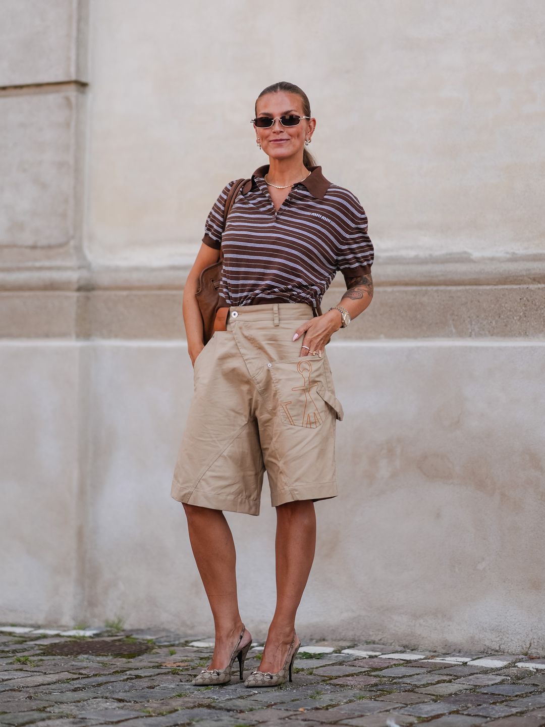 Janka Polliani wears a light grey and brown striped polo with beige Bermudas and logo emblazoned slingbacks outside The Garment at Copenhagen Fashion Week.