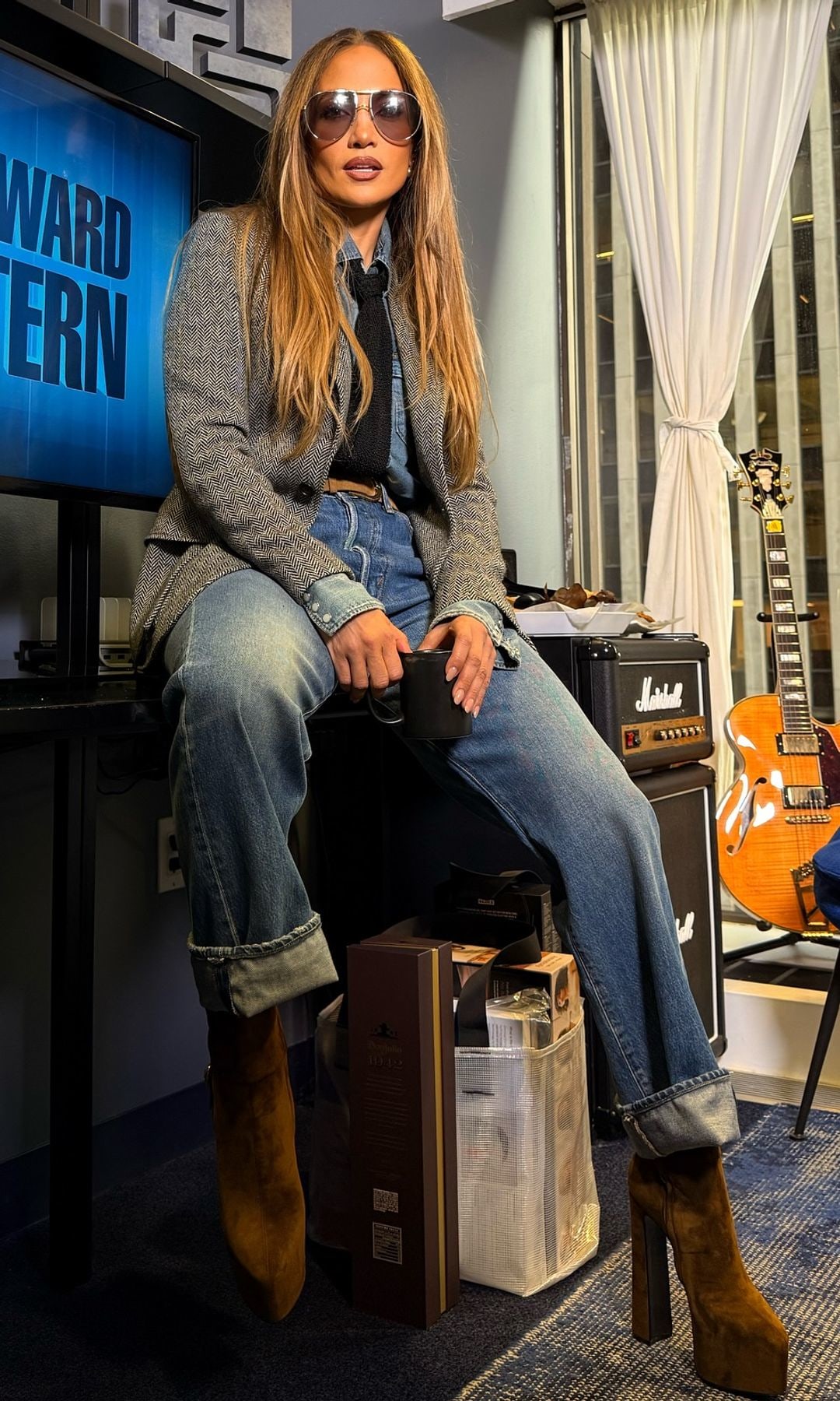 Jennifer Lopez sits on a table wearing jeans and platform brown boots