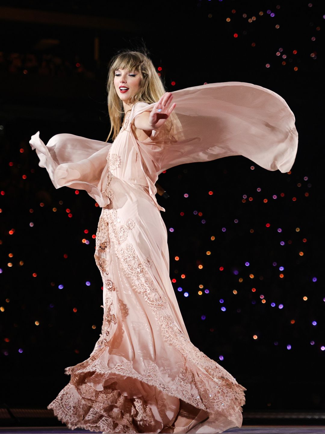Taylor Swift on stage surrounded by hundreds of fans, her light pink dress billowing behind her