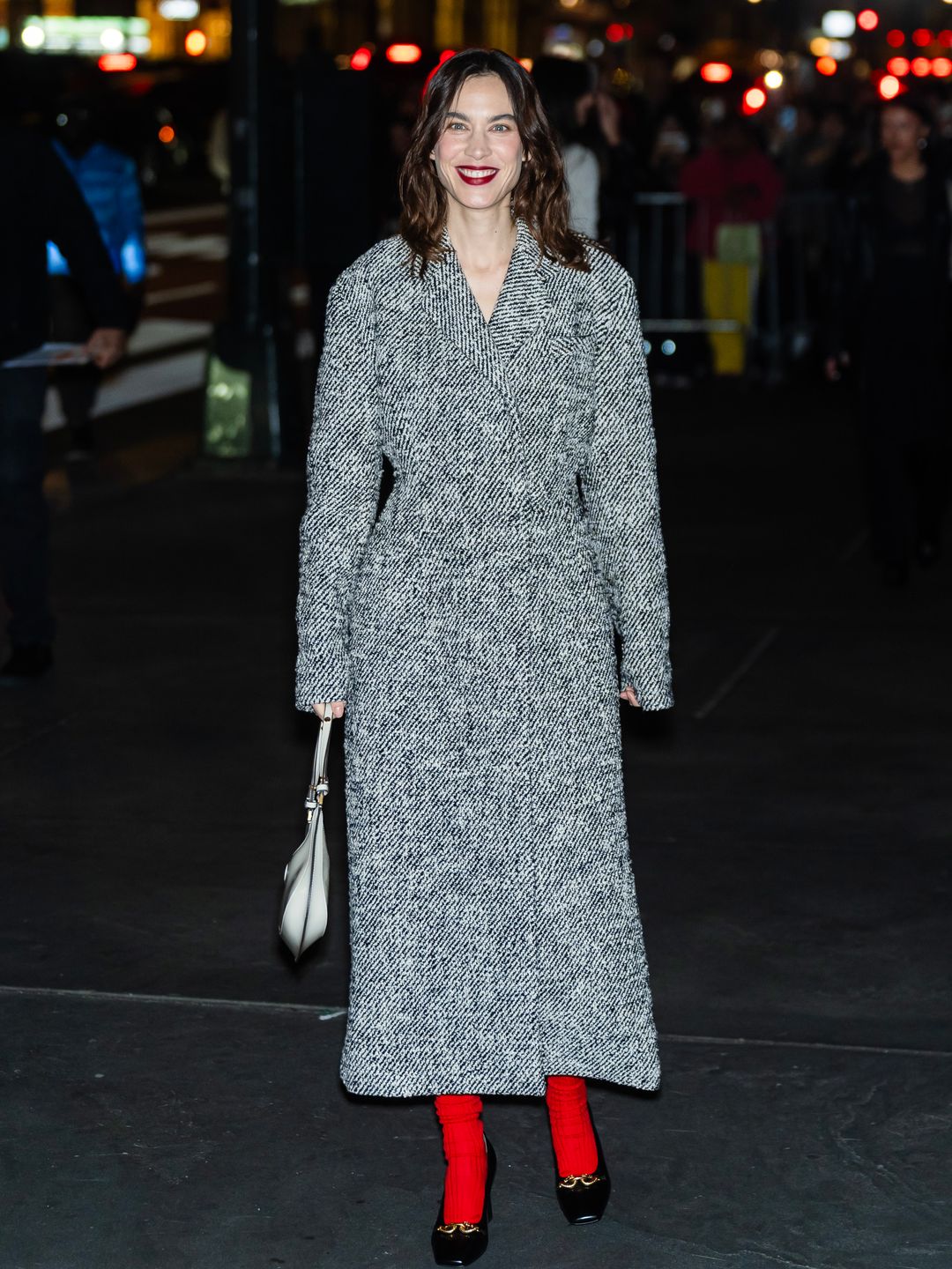 Alexa Chung attends the Tory Burch fashion show in a long grey coat with red socks and black heels 