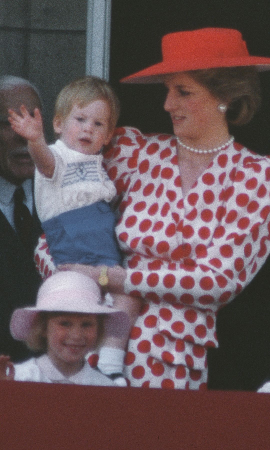 Princess Diana in red holding Prince Harry in blue shorts