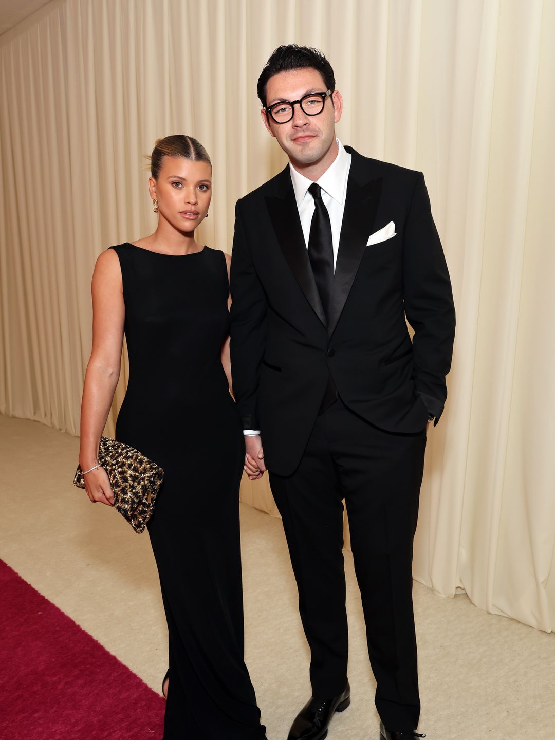 Sofia Richie in a black dress and Elliot Grainge in a suit and glasses