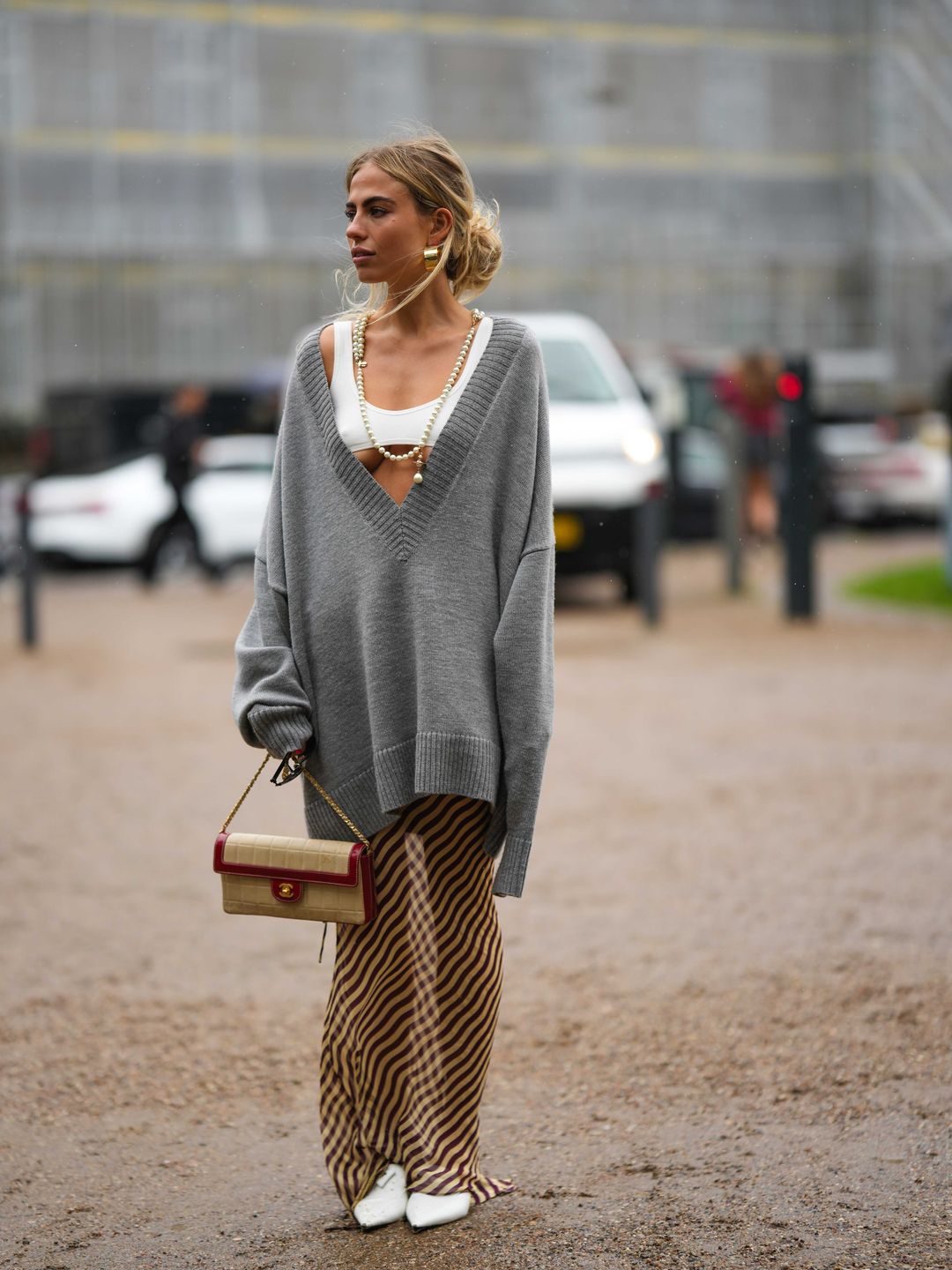A stylish guest wearing a white micro top, a grey oversized jumper and a striped sheer skirt 