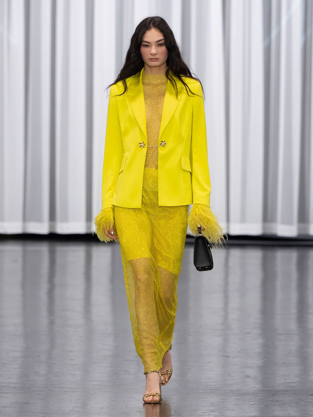 Marc Cain sends a model downt he cat walk in a all-yellow crystal encrusted sheer maxi dress with feather cuffs and a matching blazer