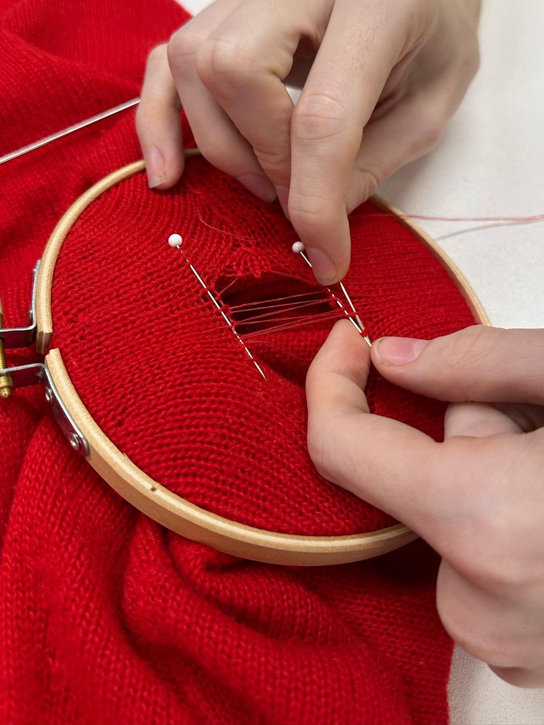 A close up image of hands repairing red knitted jumper