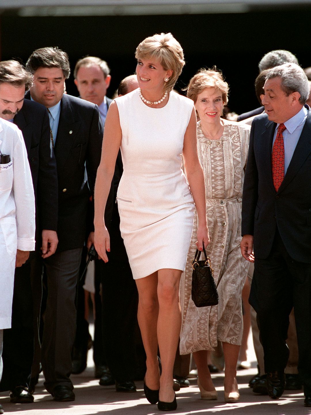 Diana, Princess Of Wales, Arriving In Argentina. The Princess Is Wearing A White Sleeveless Shift Dress Designed By Fashon Designer Versace And Carrying A Black Christian Dior Handbag.