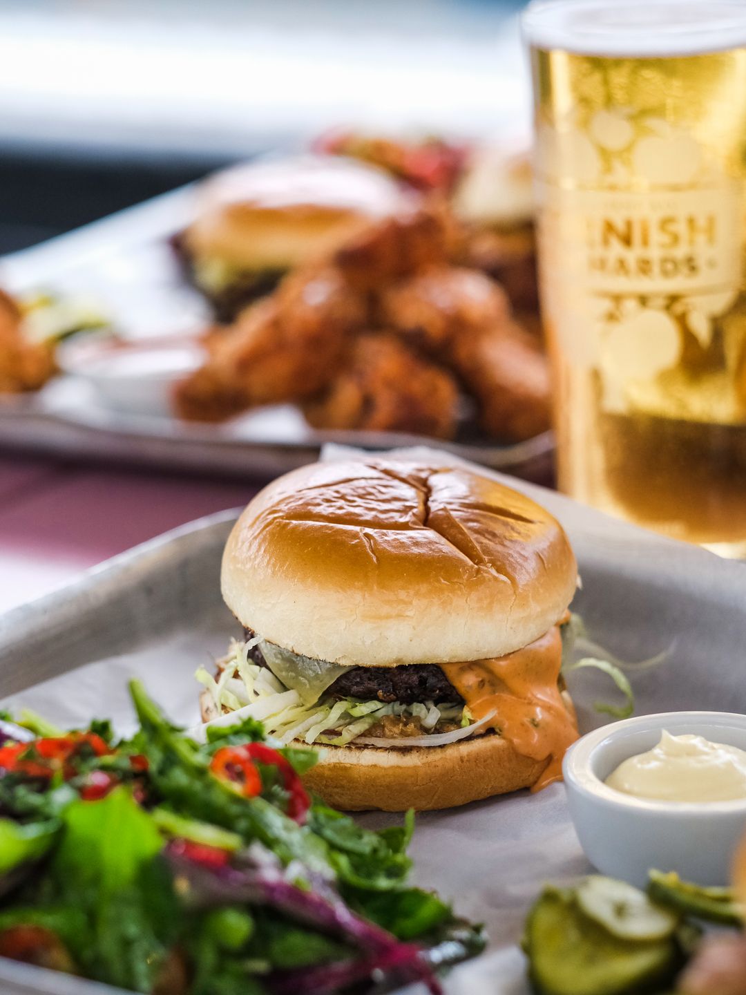 A burger from Studio Kitchen with a patty, lettuce and cheese - sides include a salad a glass of beer and a mayonnaise dip