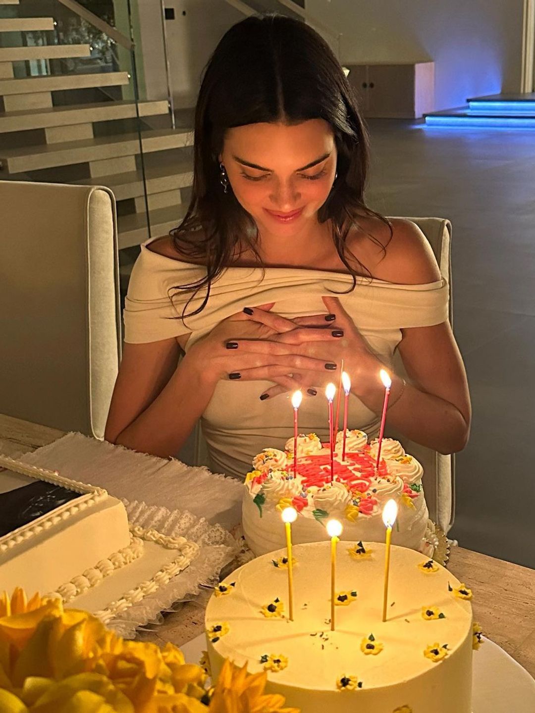 Kendall Jenner smiling over her birthday cake in a white off-the-shoulder dress