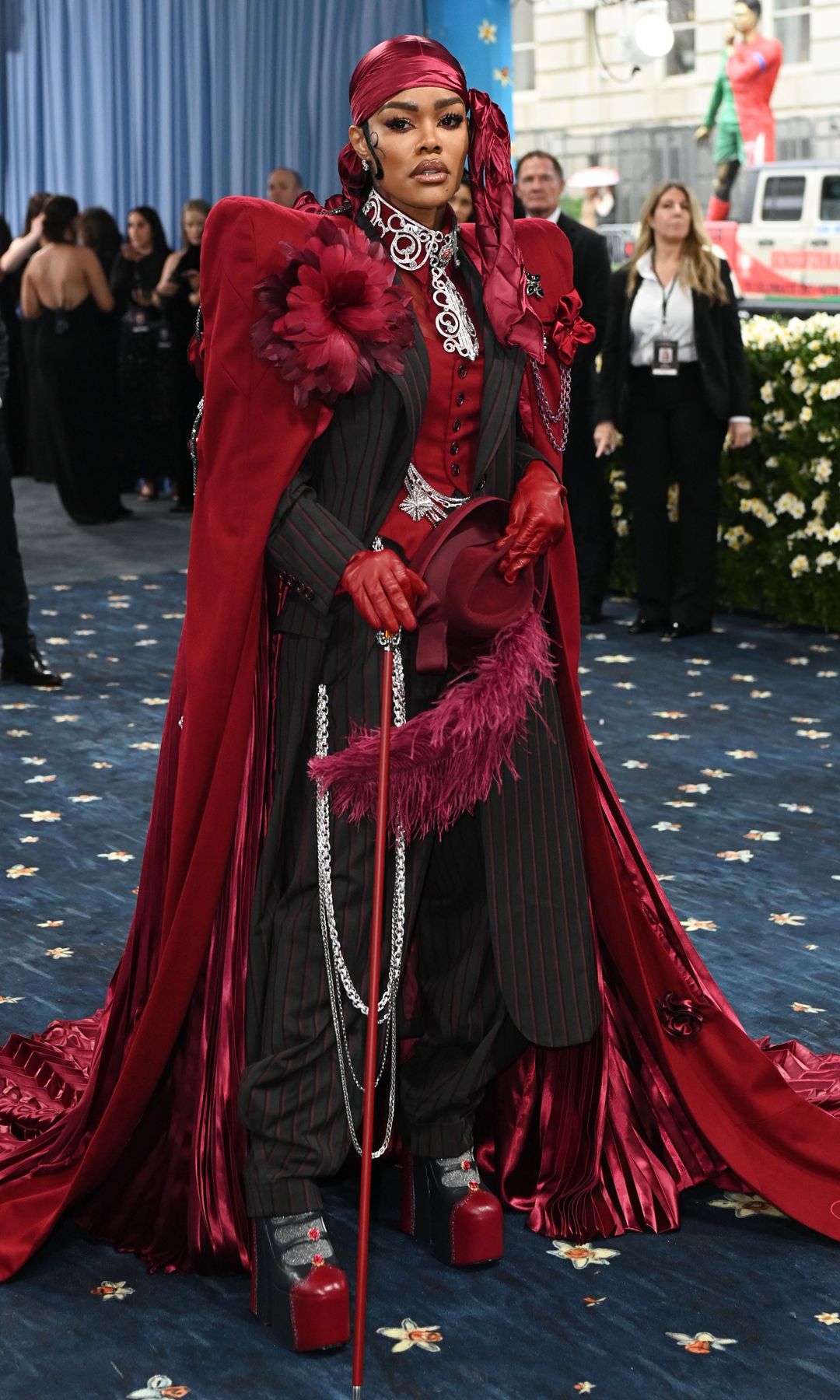 Teyana Taylor wears an elaborate black suit, with red platform shoes, headscarf, feathered cape and cane.