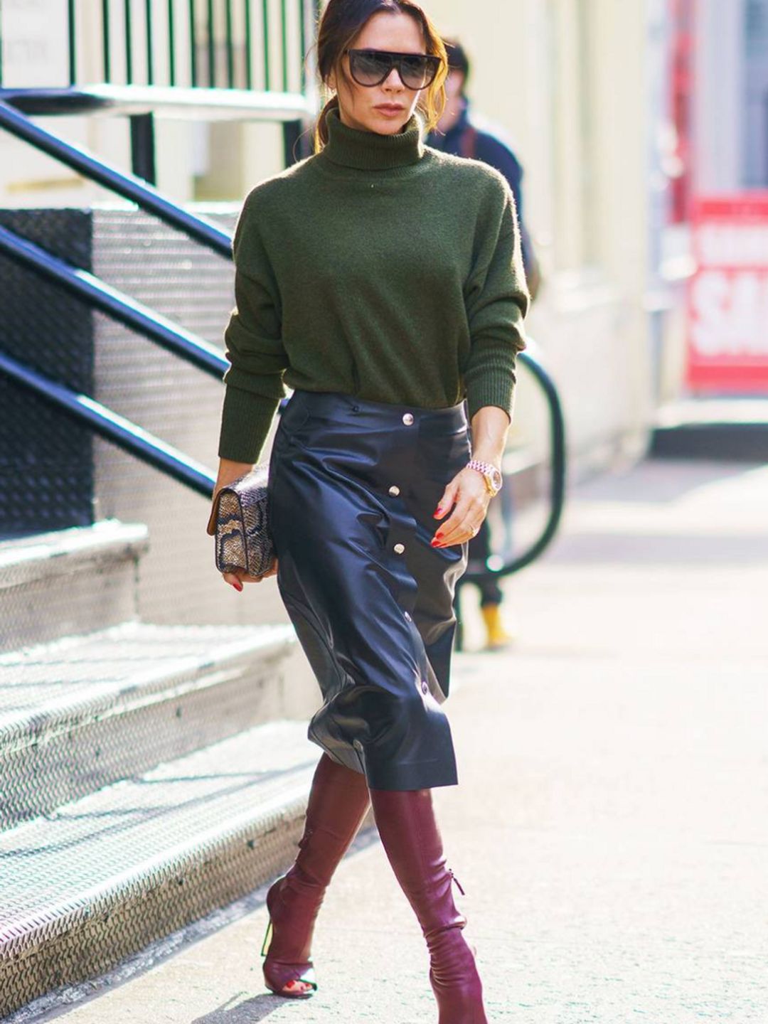 Victoria Beckham wears a leather midi skirt, green sweater and burgundy boots
