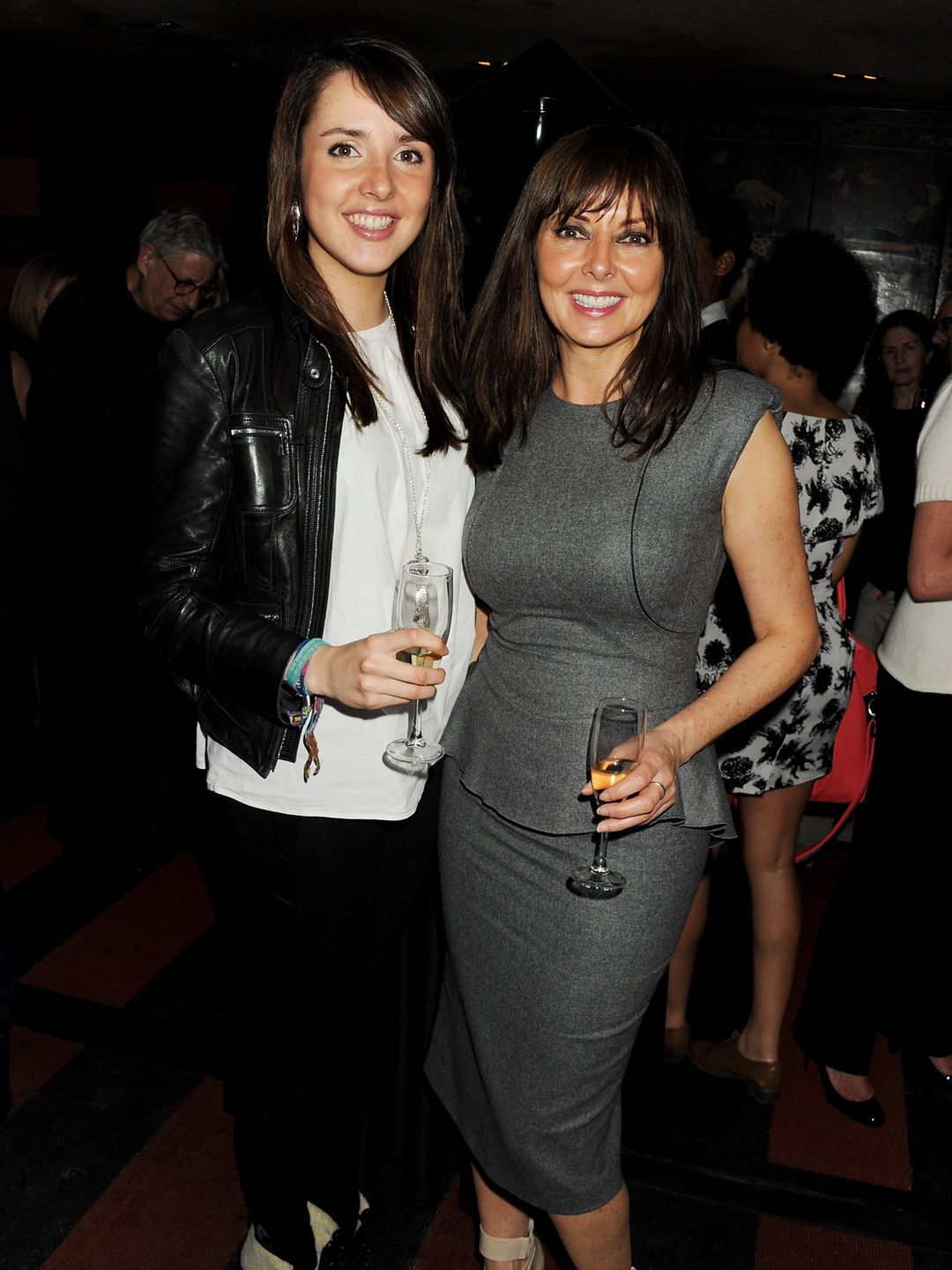 Carol Vorderman in a grey dress and daughter Katie in a black leather jacket, white shirt and black trousers - both hold glasses