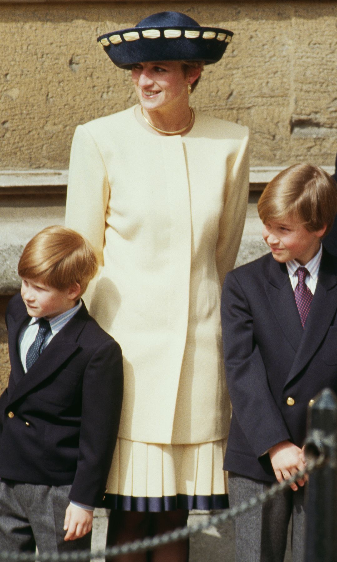 Princess Diana stands beside Prince Harry, Prince William, and Princess Anne in her iconic butter yellow suit, radiating elegance at the 1992 royal Easter service outside St. George’s Chapel.