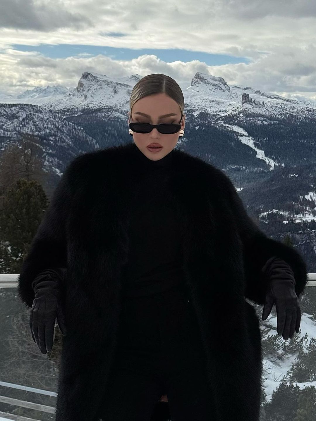 Influencer @romaneinnc wears a black fur coat, leather black gloves and oval sunglasses on holiday in the mountains