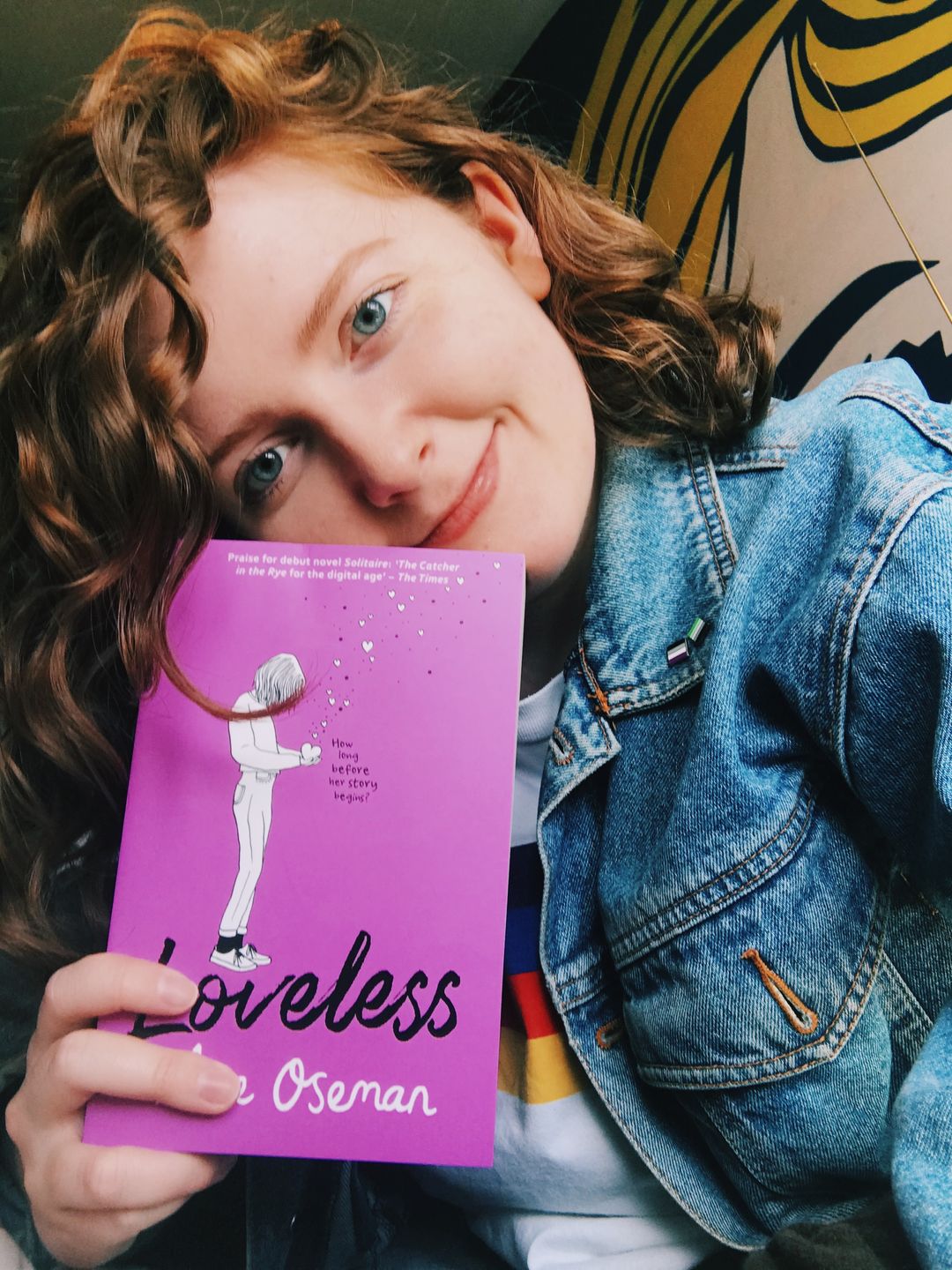 Alice smiling for a selfie, holding up her new book (which is purple) against her cheek