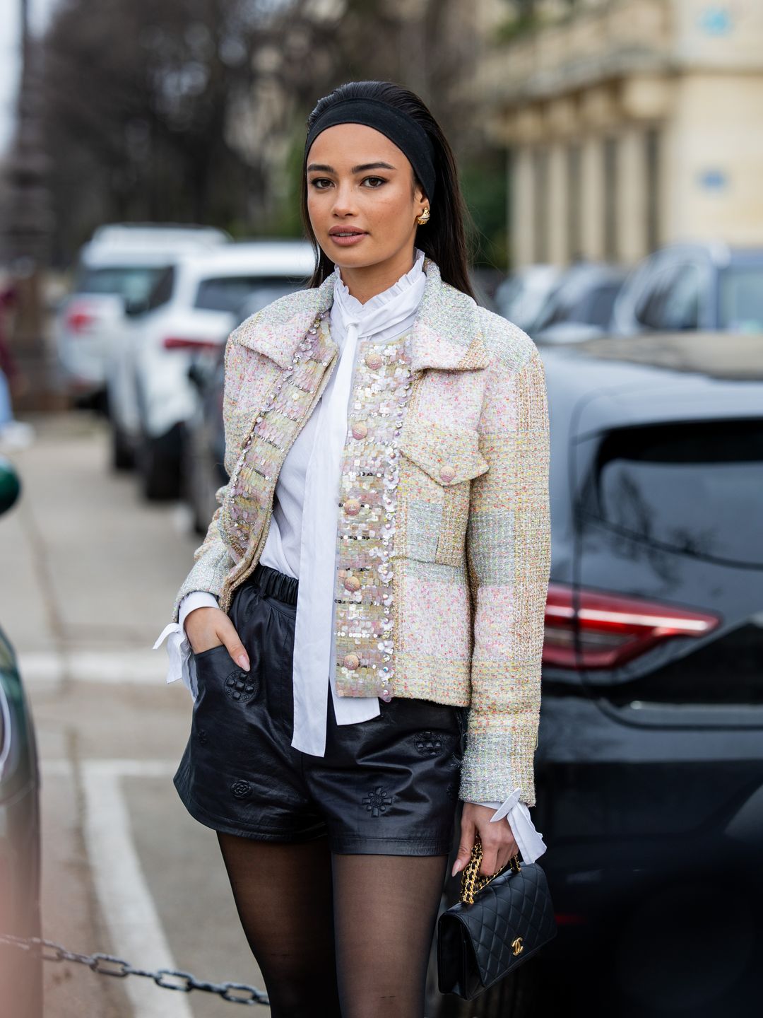 Kelsey Merritt wears hair band, black leather shorts, tights, bag, white blouse, jacket outside Chanel during the Haute Couture Spring/Summer 2024