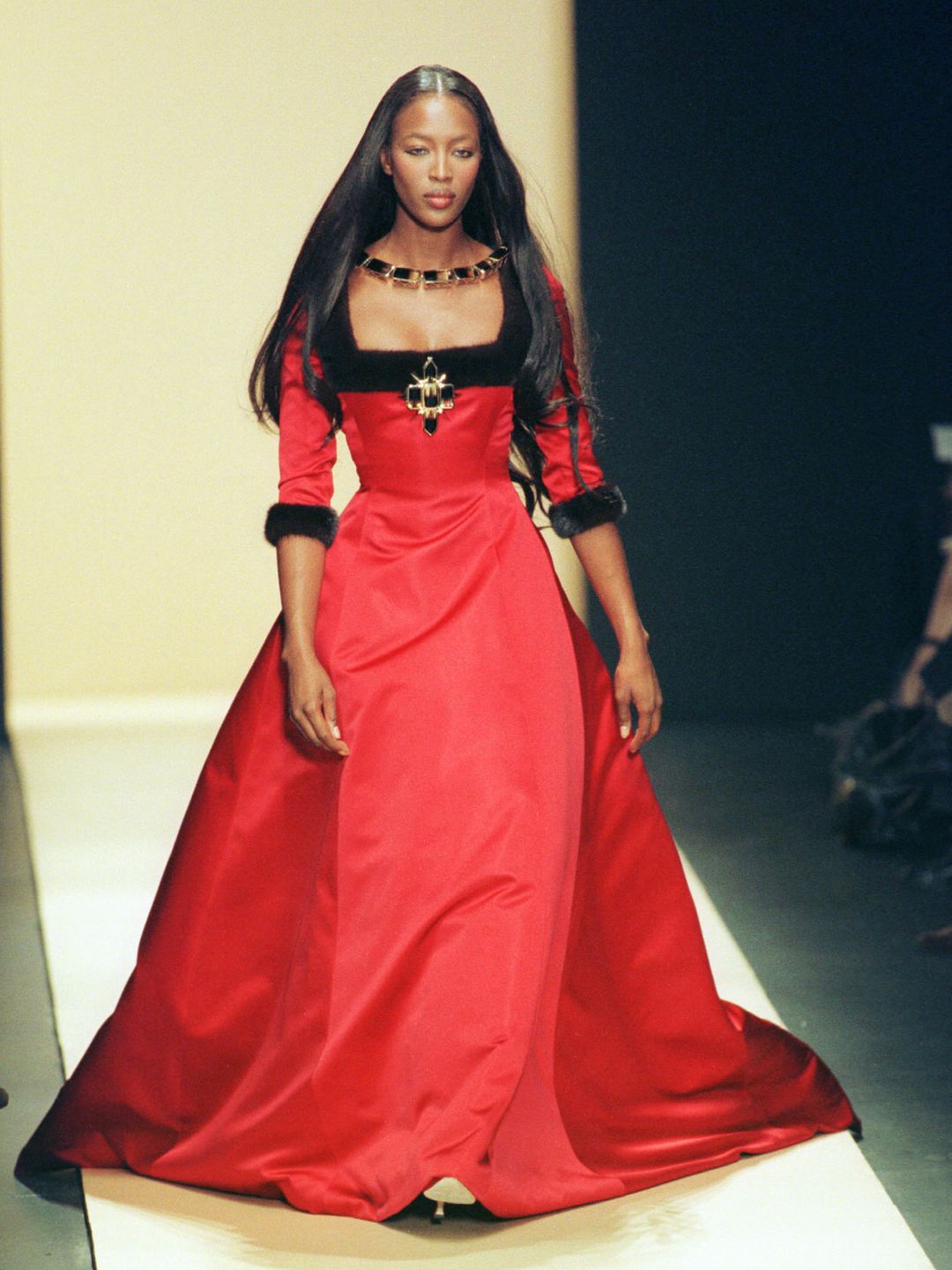 Naomi Campbell wearing a Tudor-esque red square-neck maxi dress with a wide skirt 