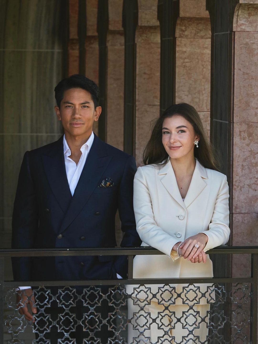 A princesa Anisha Rosnah de Brunei posa em um terno branco em uma varanda ao lado de seu marido, o príncipe Mateen 