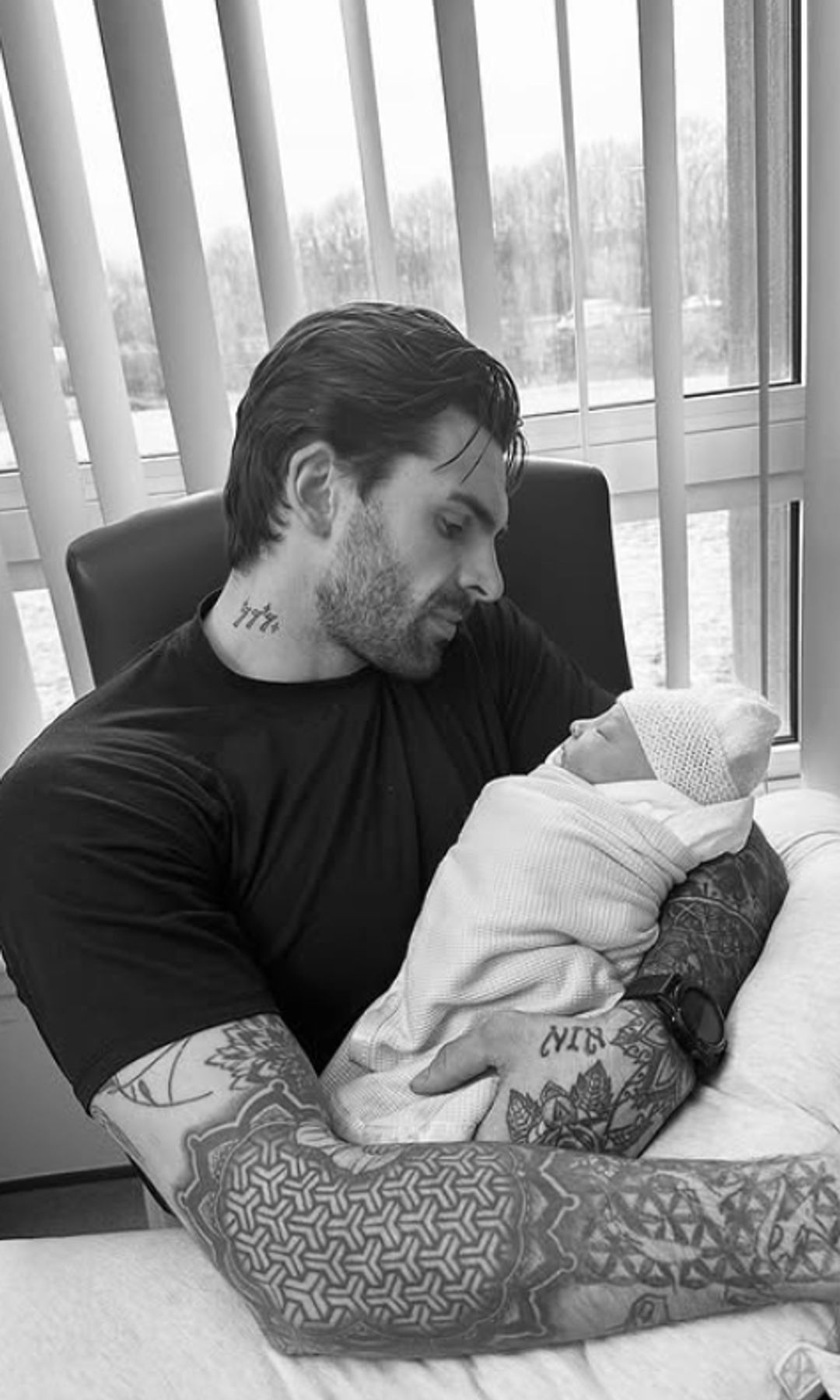 Black-and-white photo of Adam Collard holding a baby that's swaddled up