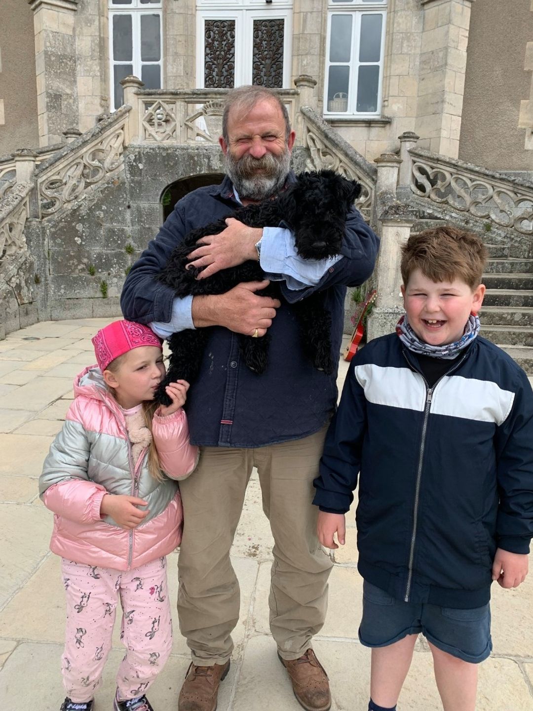 father holding dog next to two children