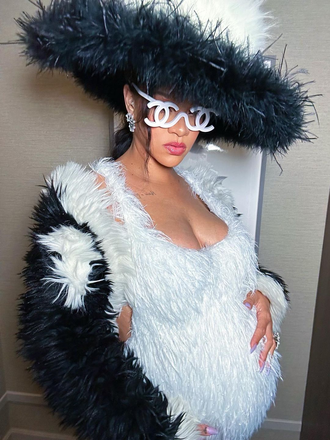 Rihanna wears a bacl and white feather outfit and large brim hat with Chanel logo sunglasses