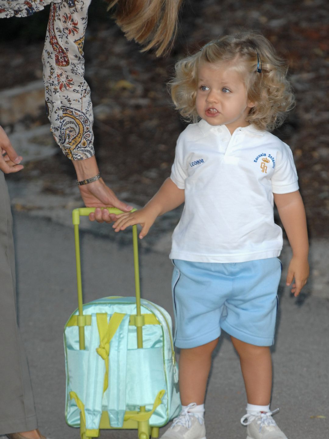 Princess Leonor in a white shirt and blue shorts carrying a small suitcase