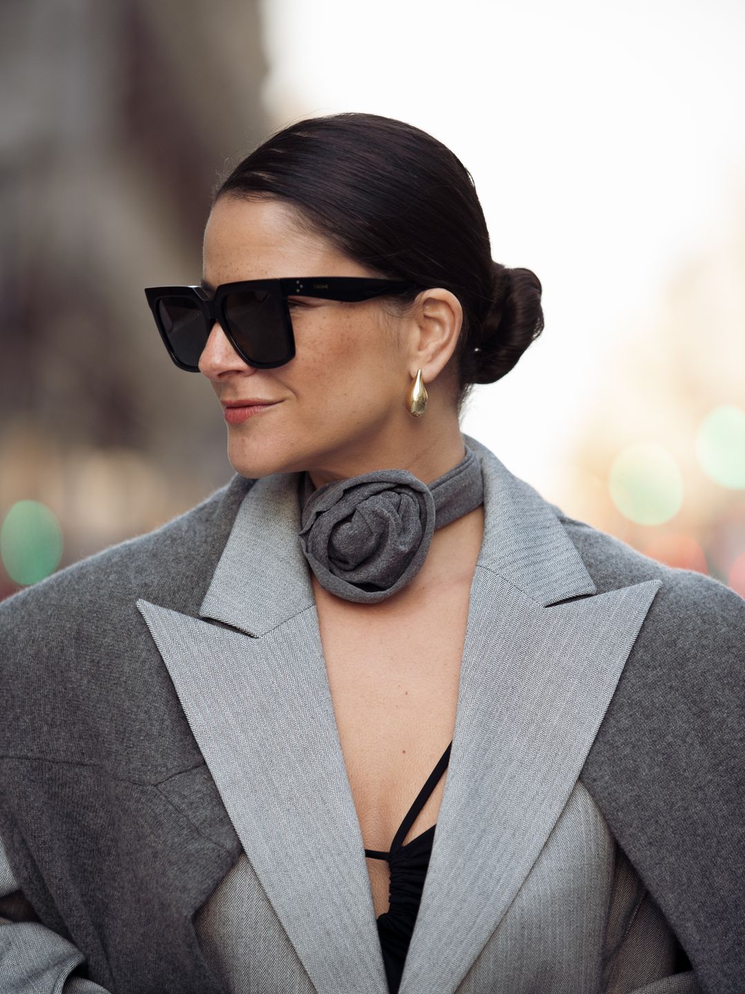 Gili Biegun wears black mini skirt, black top, grey cropped jacket, grey sweater over the shoulders, grey neck accessory flower rose from fabric, and green bag during the Womenswear Fall/Winter 2024/2025 as part of  Paris Fashion Week