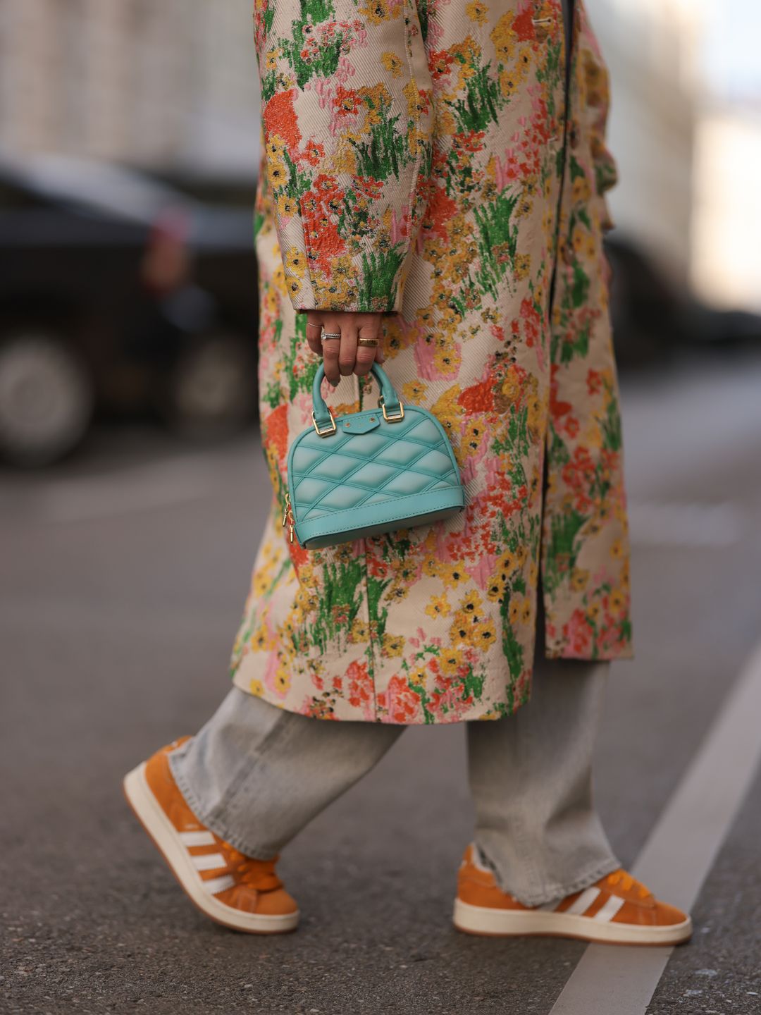 Karin Teigl seen wearing Agolde light grey denim straight leg pants, Stine Goya yellow with colorful flower embroidered pattern long coat and a  Louis Vuitton light blue leather Alma mini bag