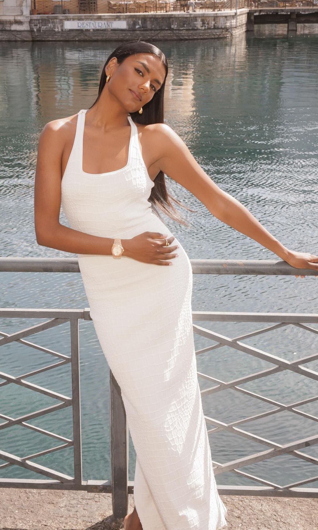 Simone Ashley poses next to a river in a white maxi dress