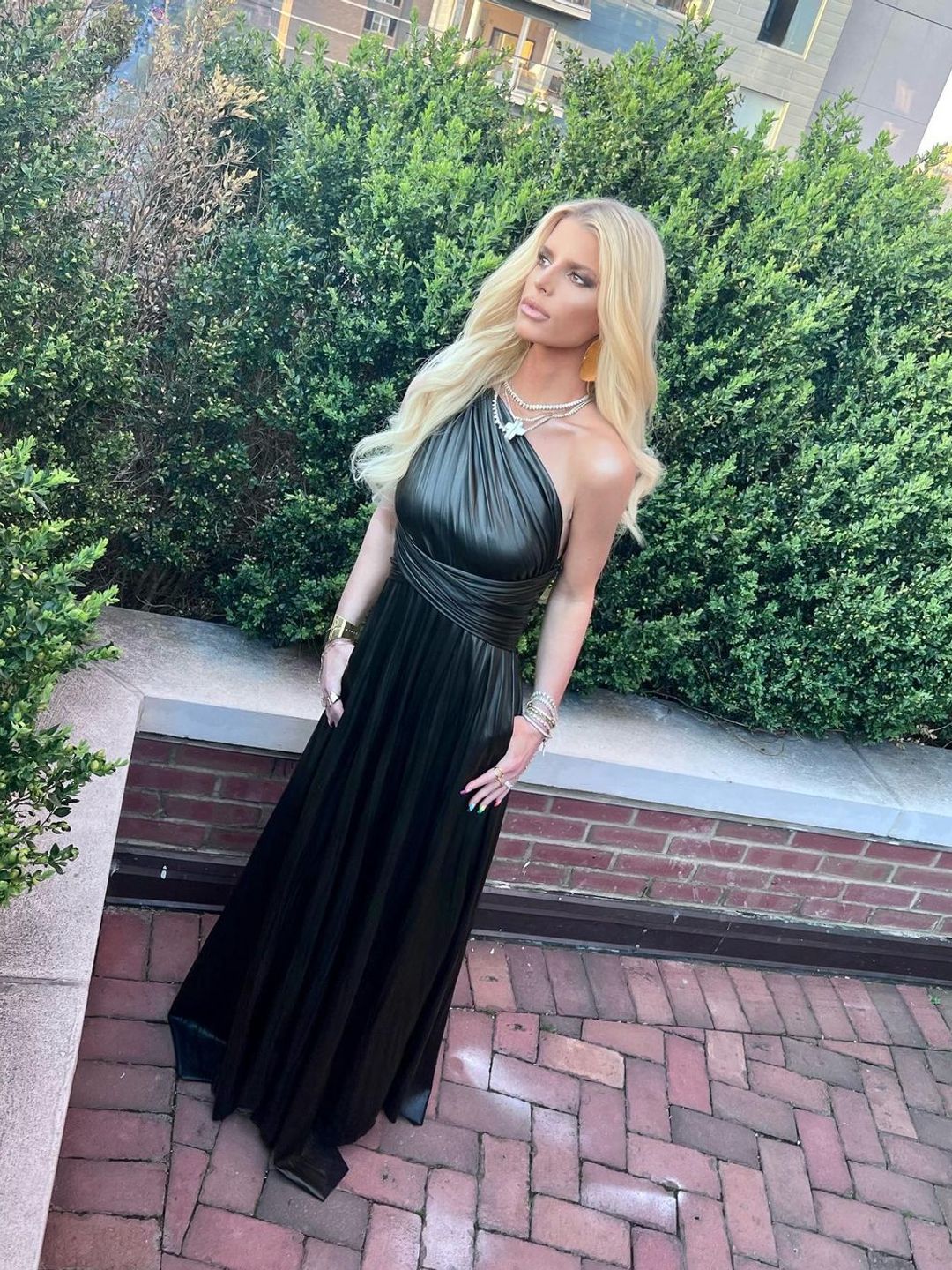 Jessica Simpson standing on a balcony in a black one-shouldered dress