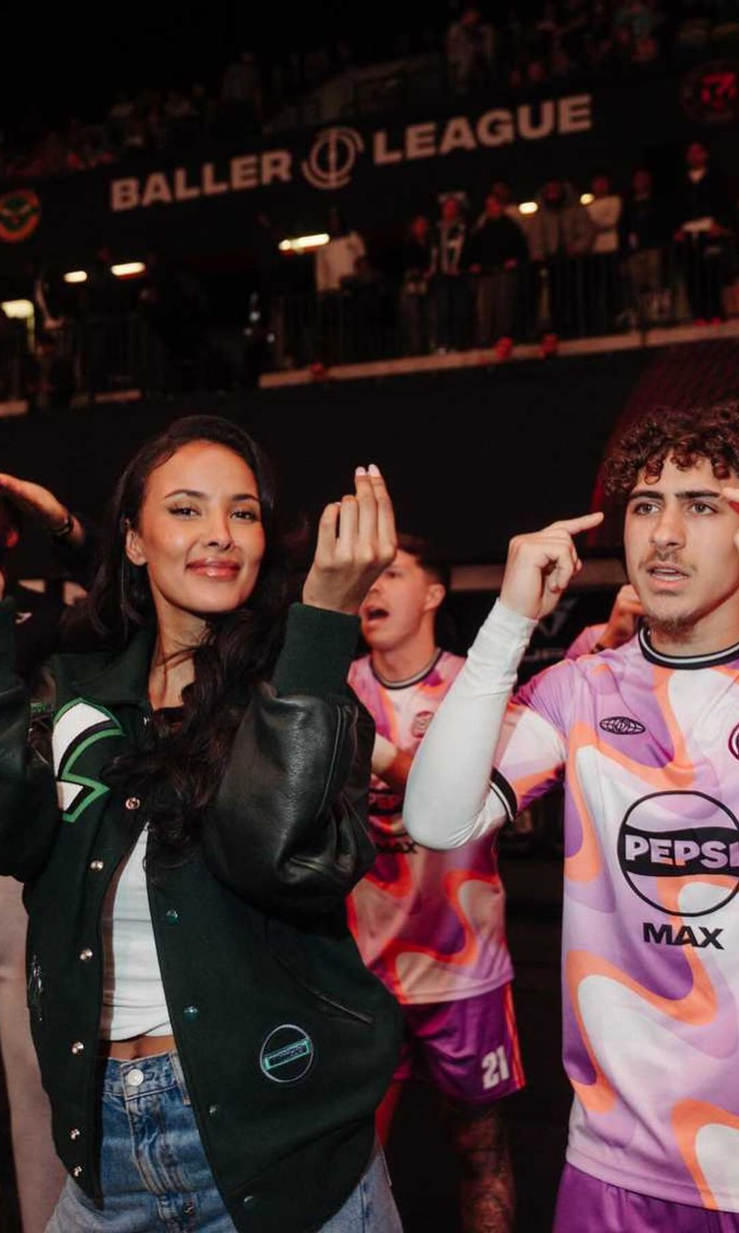 Maya Jama poses with a football player on the sideline of the indoor pitch