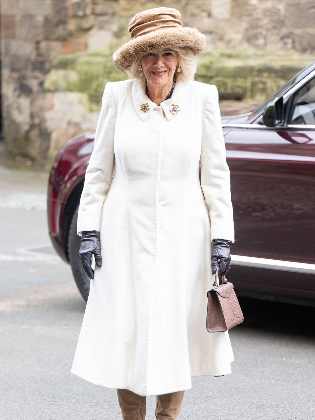 Rainha Camilla usando seu vestido casaco Fiona Clare ao lado de um luxuoso acessório de alça superior 