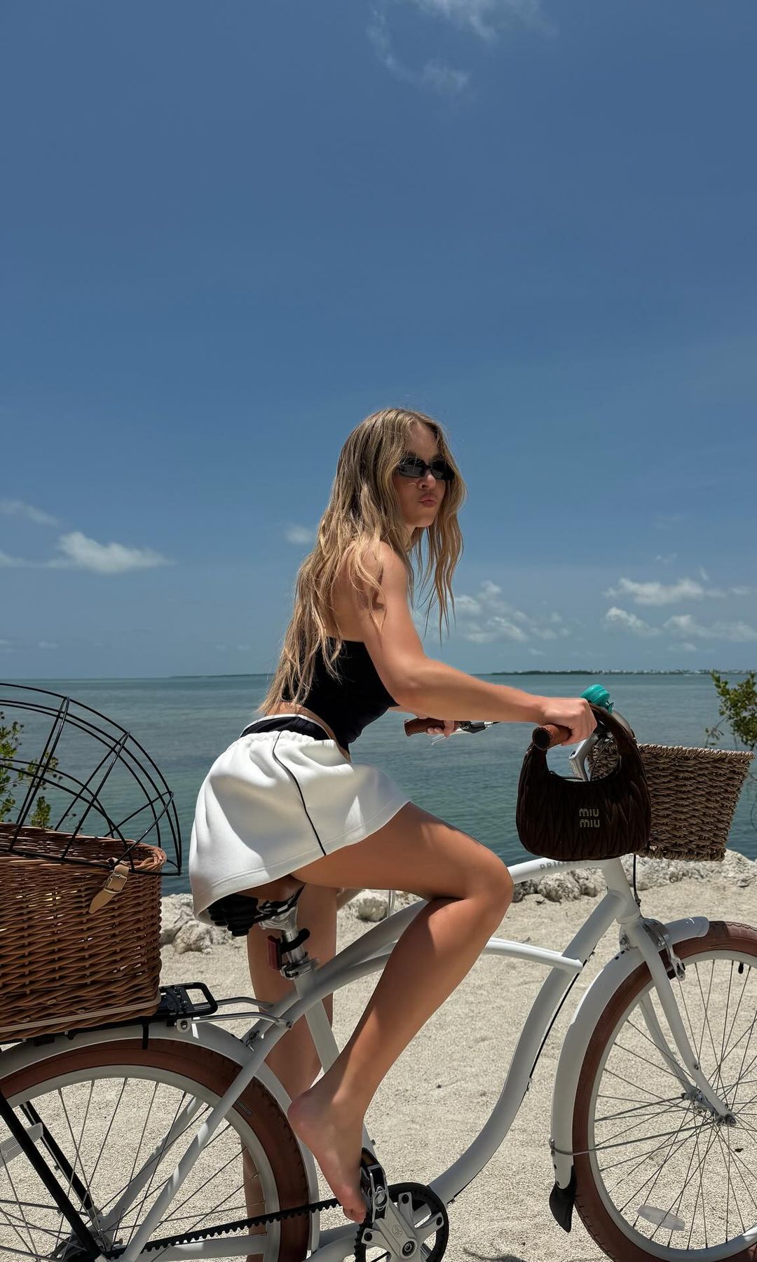 Syndey Sweeney poses in a white mini skirt and navy crop top on a bike while on holiday