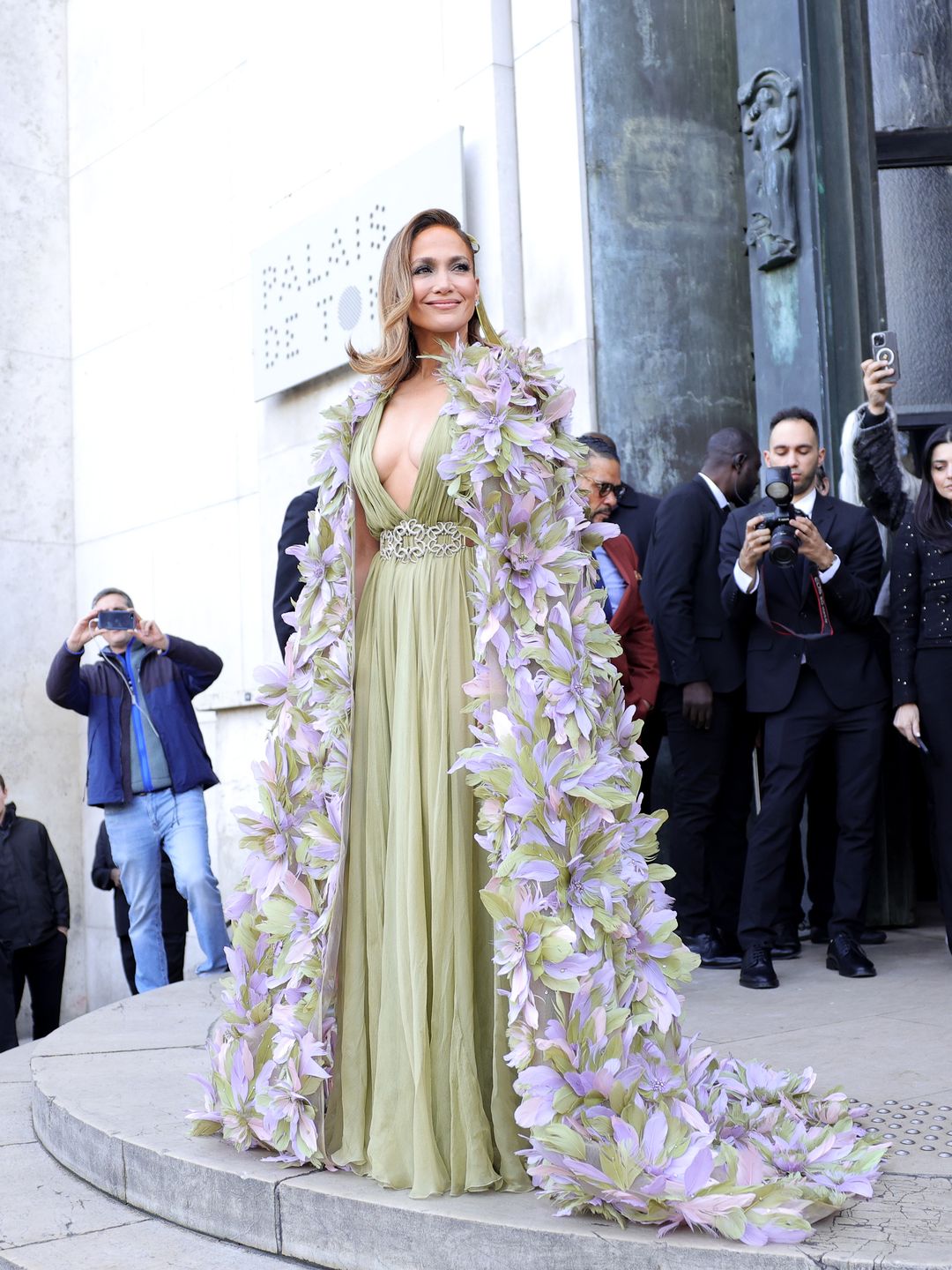Jennifer Lopez attends the Elie Saab Haute Couture Spring/Summer 2024 in asage green gown, feather flowered cape and a velvet hair bow 