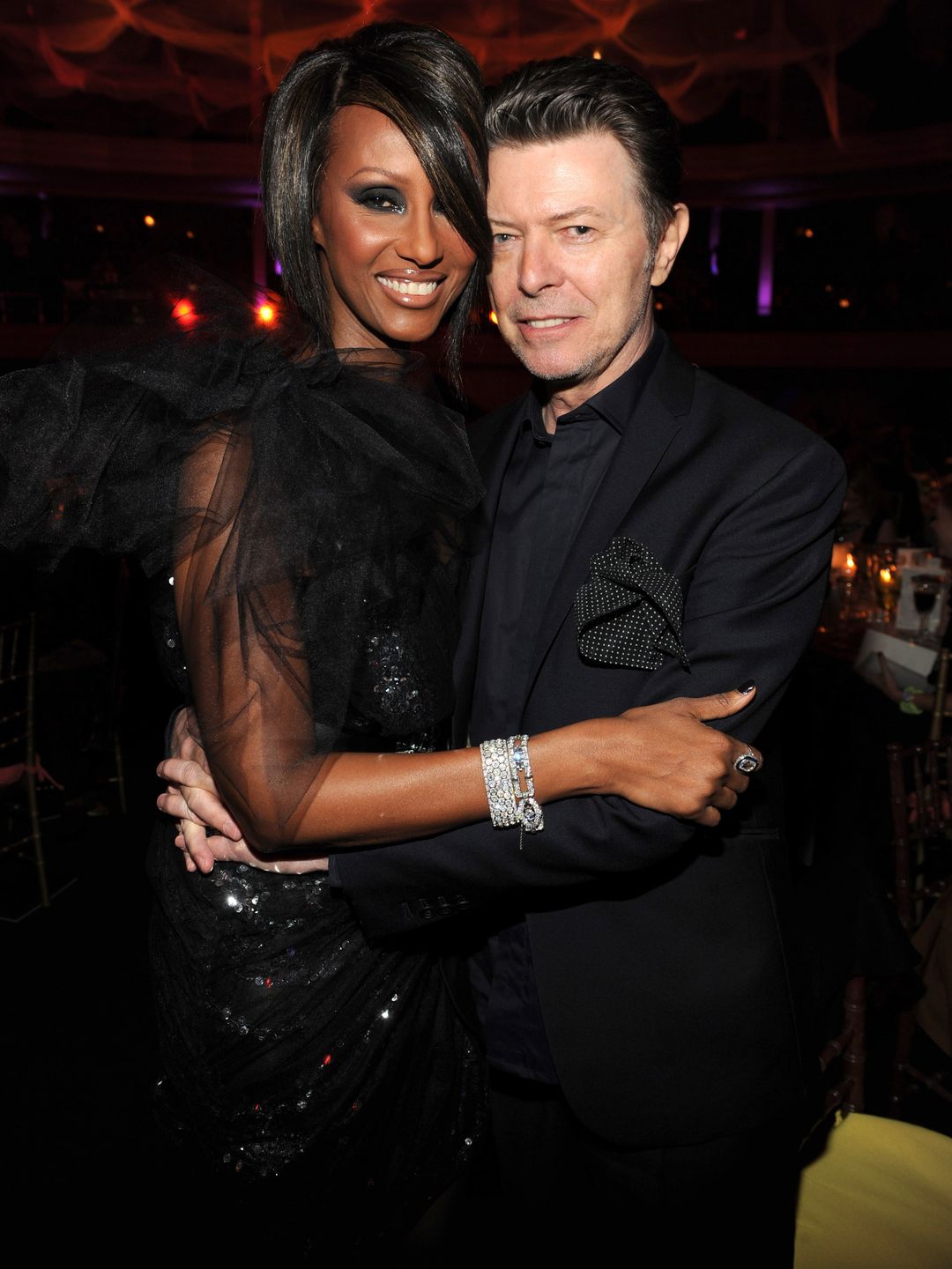 Iman and David Bowie hugging in black outifts