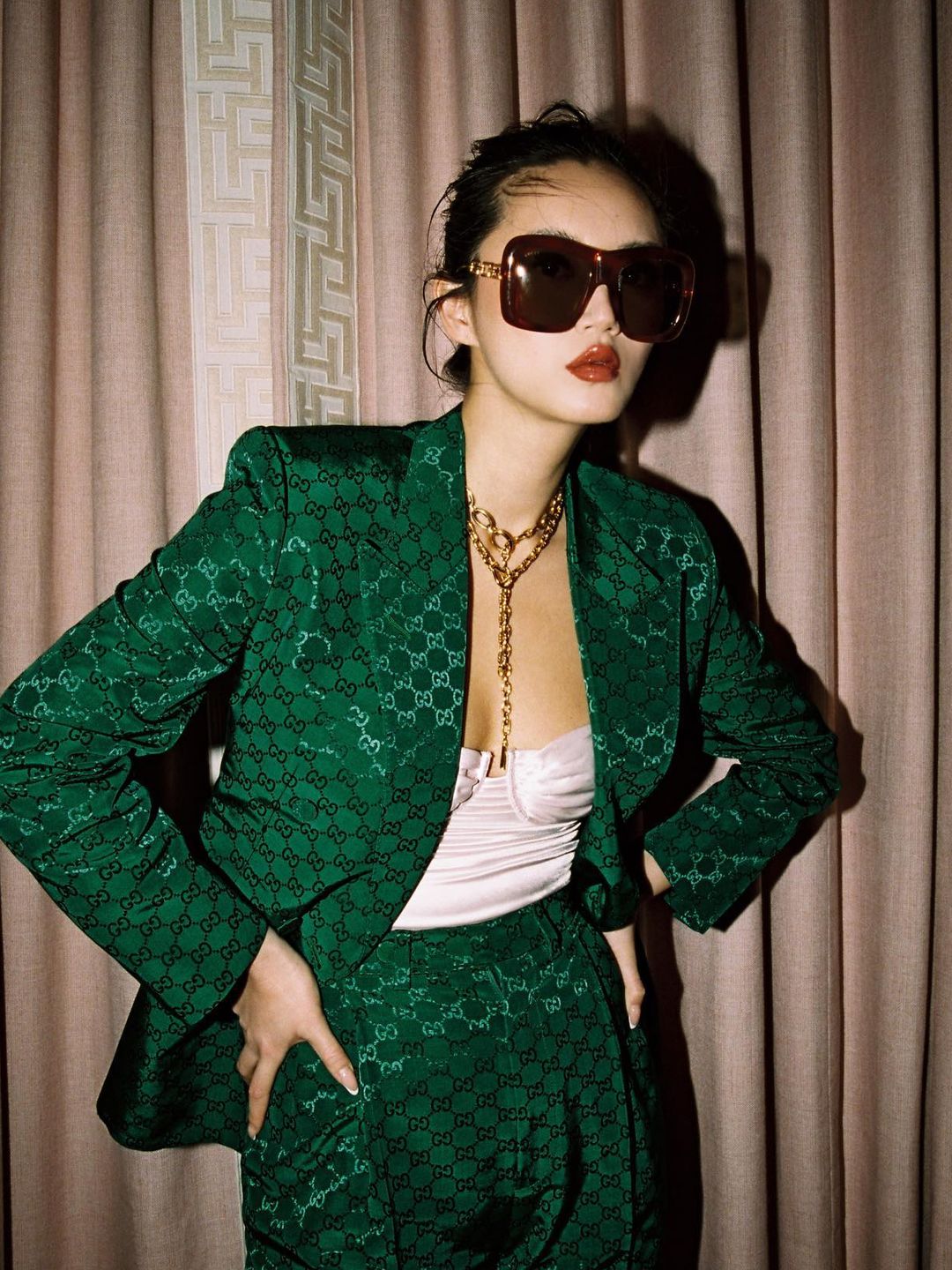 Betty Bachz wears a green guicci suit with a white corset and oversized sunglasses