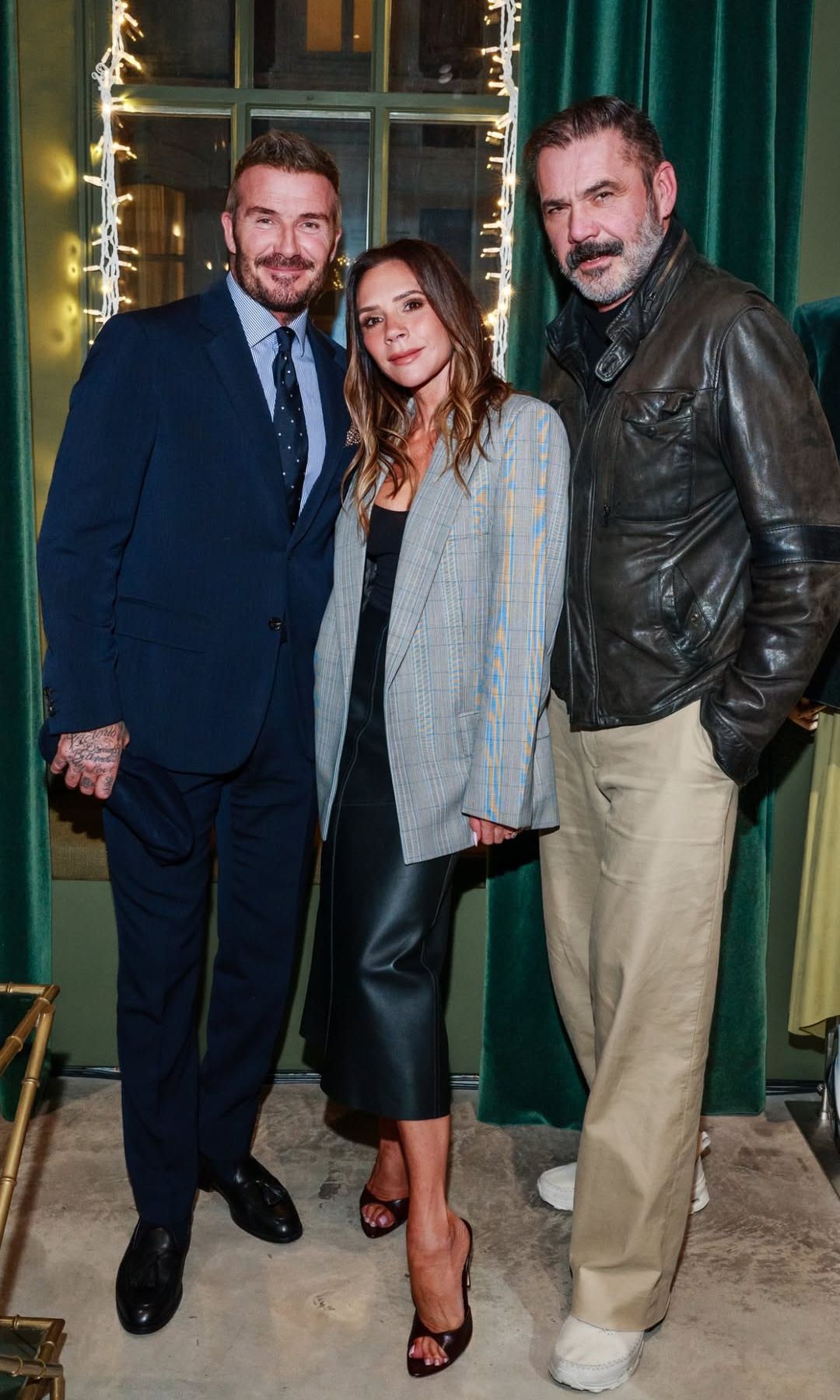 Victoria Beckham poses with a friend in front of a Christmas tree wearing a checkered blazer and leather midi skirt 