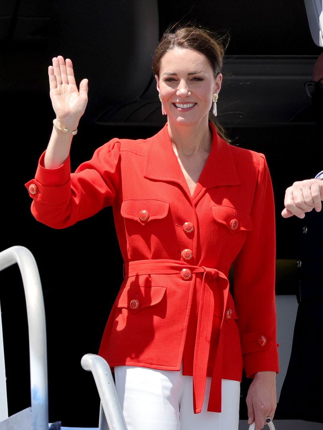 Kate Middleton in an orange coat and white trousers waving from an aeroplane