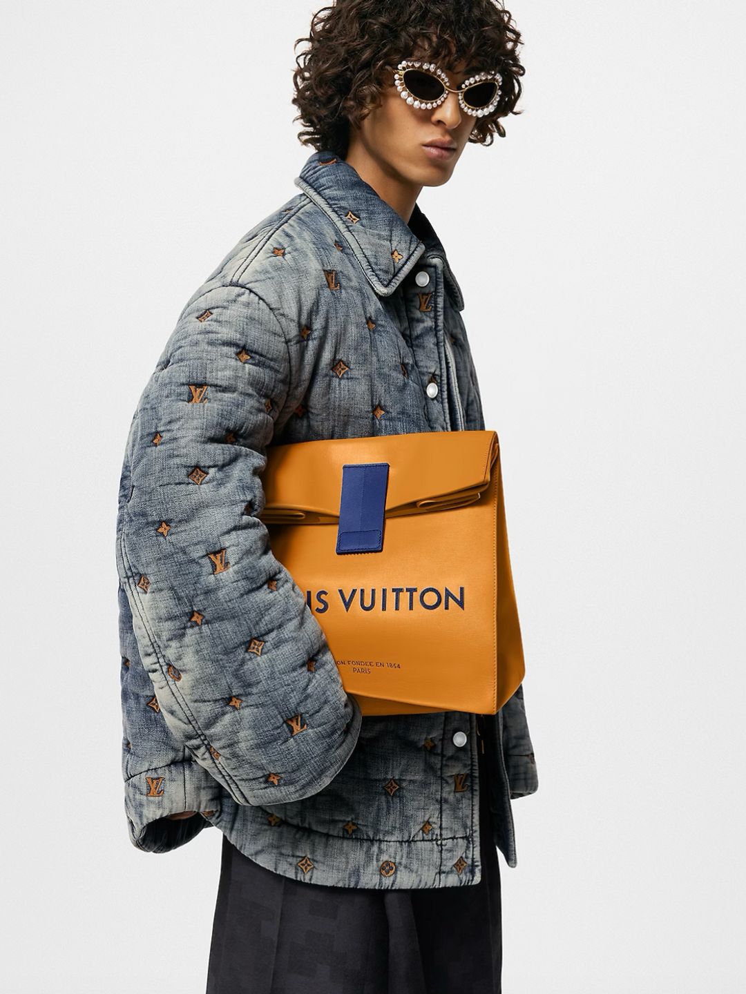 A model wearing a oversized denim jacket poses with the Louis Vuitton leather sandwhich bag