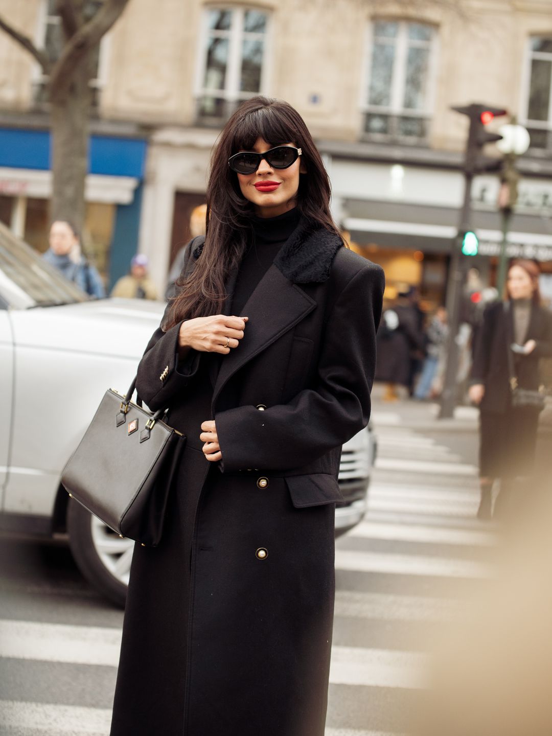 ameela Jamil wears black long coat, sunglasses and a black bag outside Casablanca during the Womenswear Fall/Winter 2024/2025